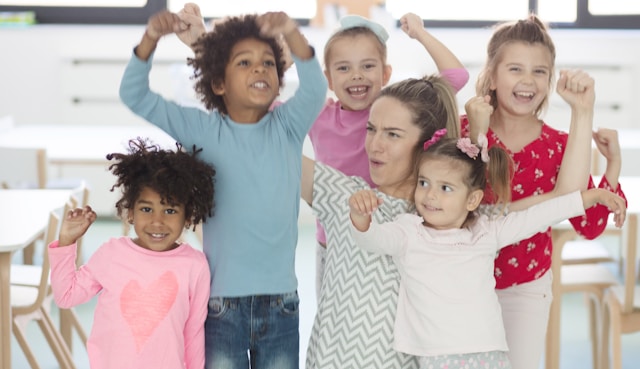 a group of happy children with their arms in the air. A teacher or mom in the middle of them.