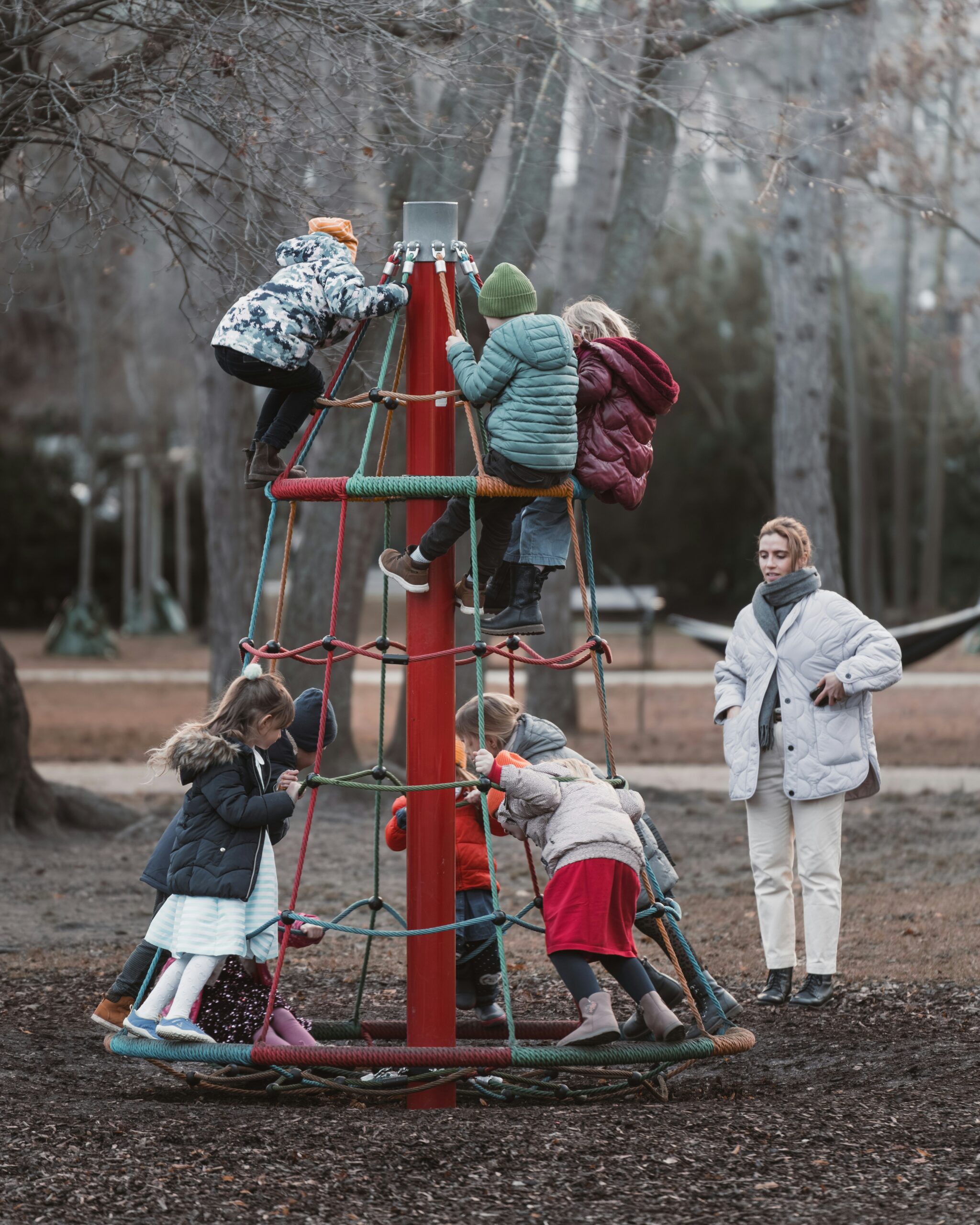 Children climbing on a play structure with an adult watching over them.