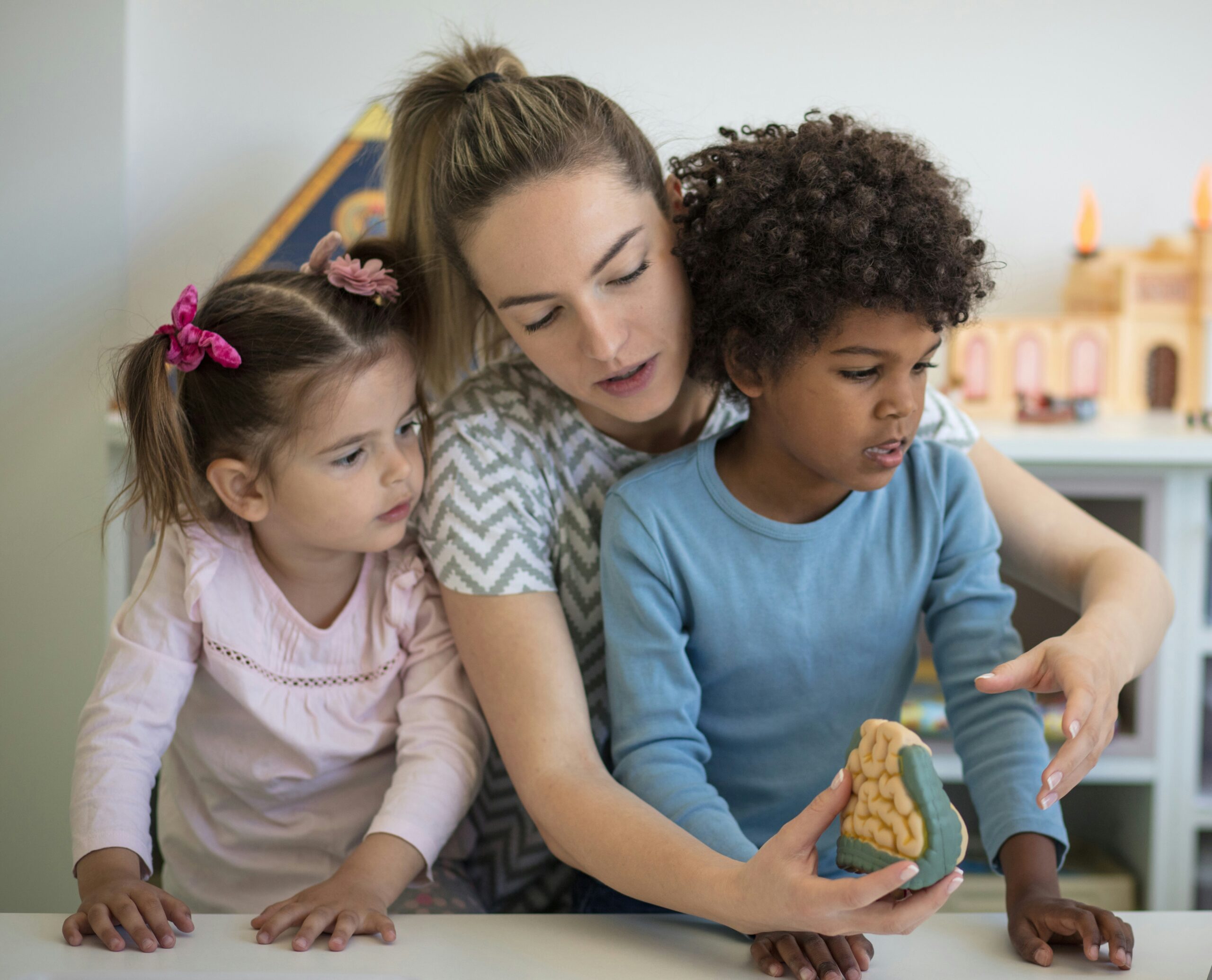 two children and adult playing with a toy brain.